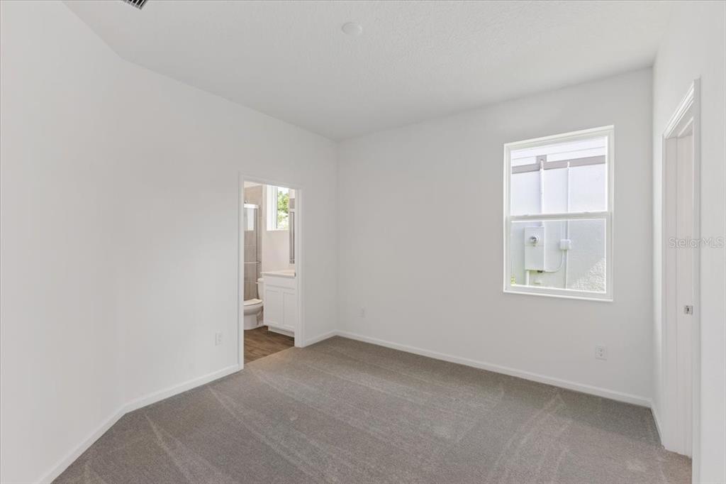 An empty bedroom with white walls, gray carpet, a single window, and an attached bathroom — 2209 SIRENA LANE, MOUNT DORA, FL