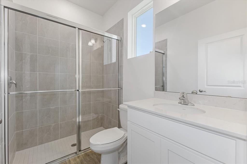A bathroom features a tiled walk-in shower, a white vanity, and a toilet — 2209 SIRENA LANE, MOUNT DORA, FL