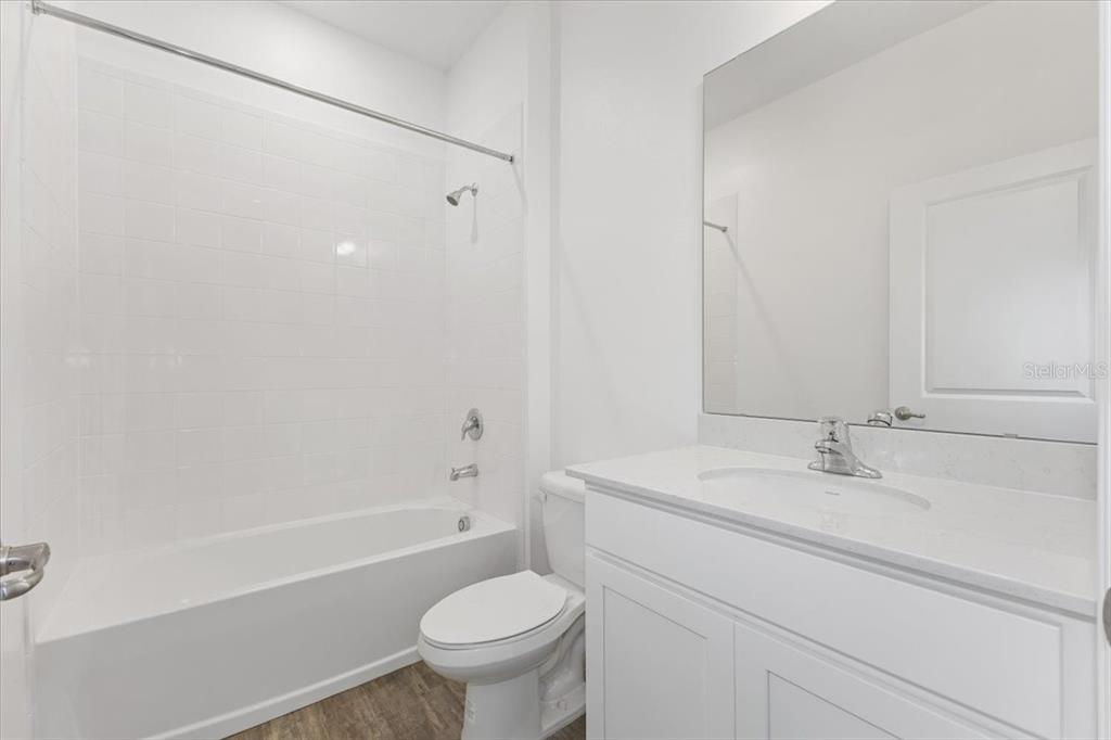 A bathroom features a white vanity, a toilet, and a shower-tub combination with white tiles — 2209 SIRENA LANE, MOUNT DORA, FL