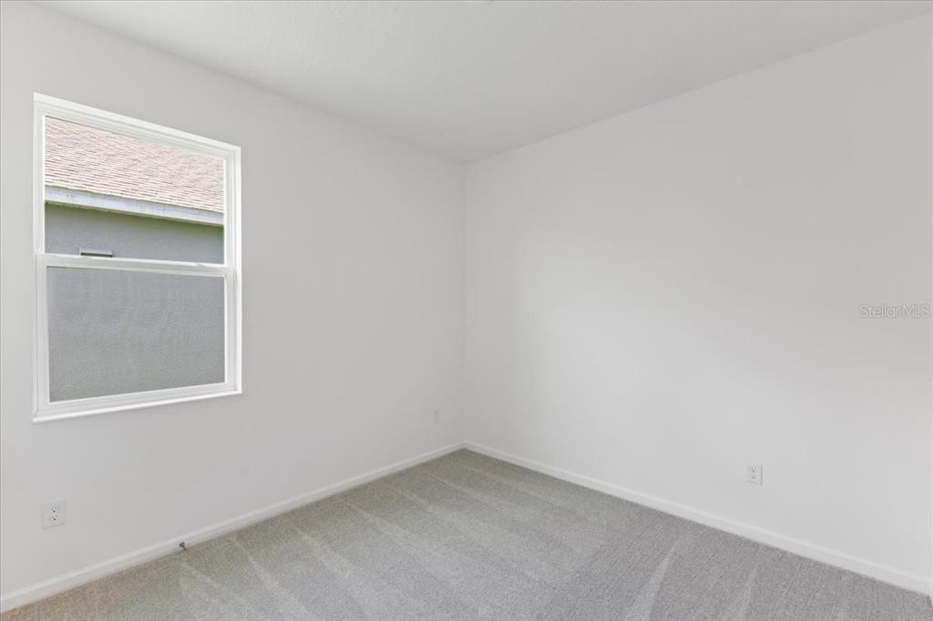 An empty bedroom features white walls, gray carpeting, and a single window — 2209 SIRENA LANE, MOUNT DORA, FL