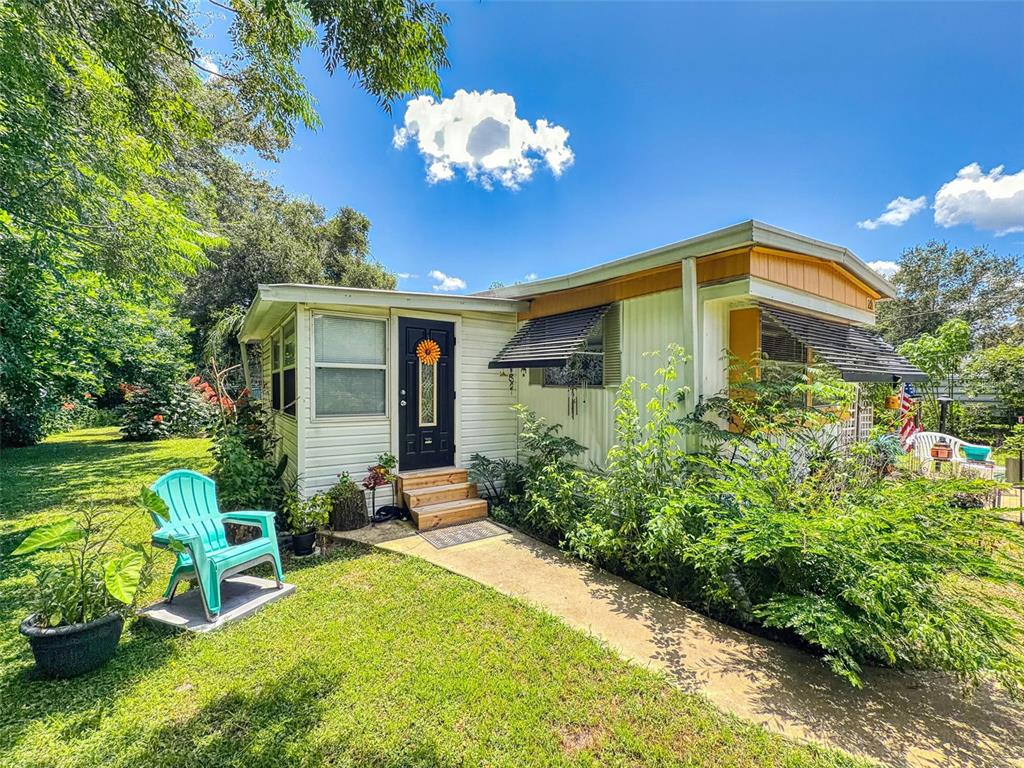 A single-story mobile home with white siding, a black front door, and a turquoise lawn chair — 221 EVERGREEN TERRACE, DELAND, FL