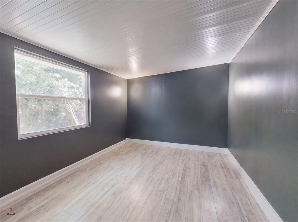 An empty room features dark gray walls, white wood-paneled ceilings, and light-colored wood-look flooring — 221 EVERGREEN TERRACE, DELAND, FL