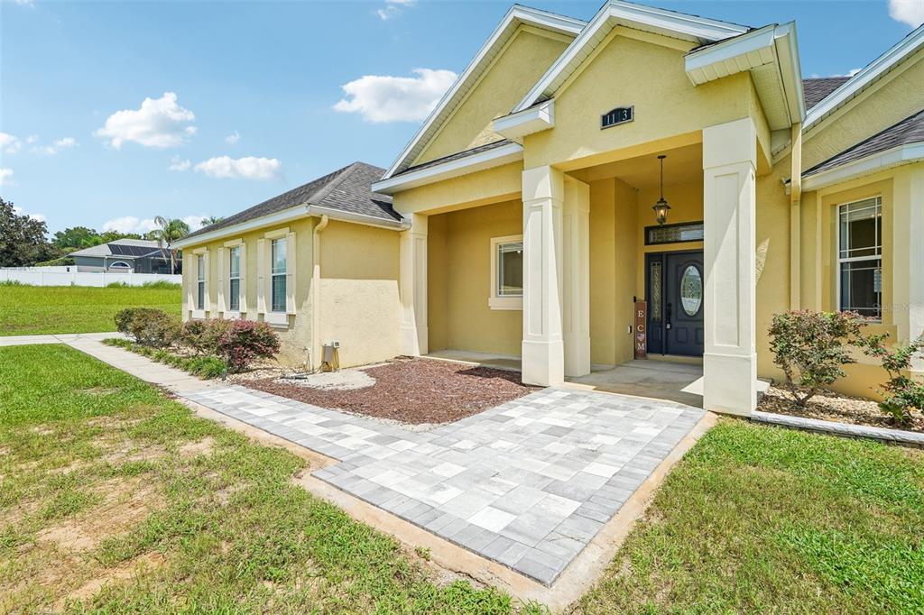 A yellow stucco house exterior features a paved walkway leading to a covered front entrance — 1113 MYRTLE BREEZES CT, FRUITLAND PARK, FL