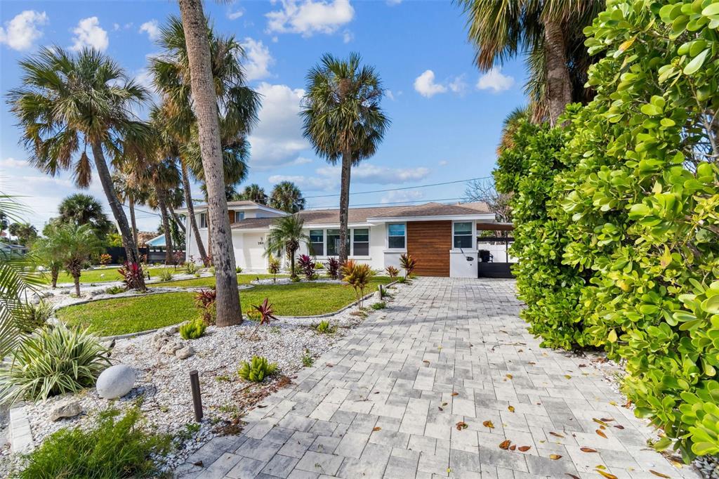 A white house with a wood-paneled accent wall features a paved driveway and palm trees — 760 BOHENIA CIRCLE S, CLEARWATER BEACH, FL