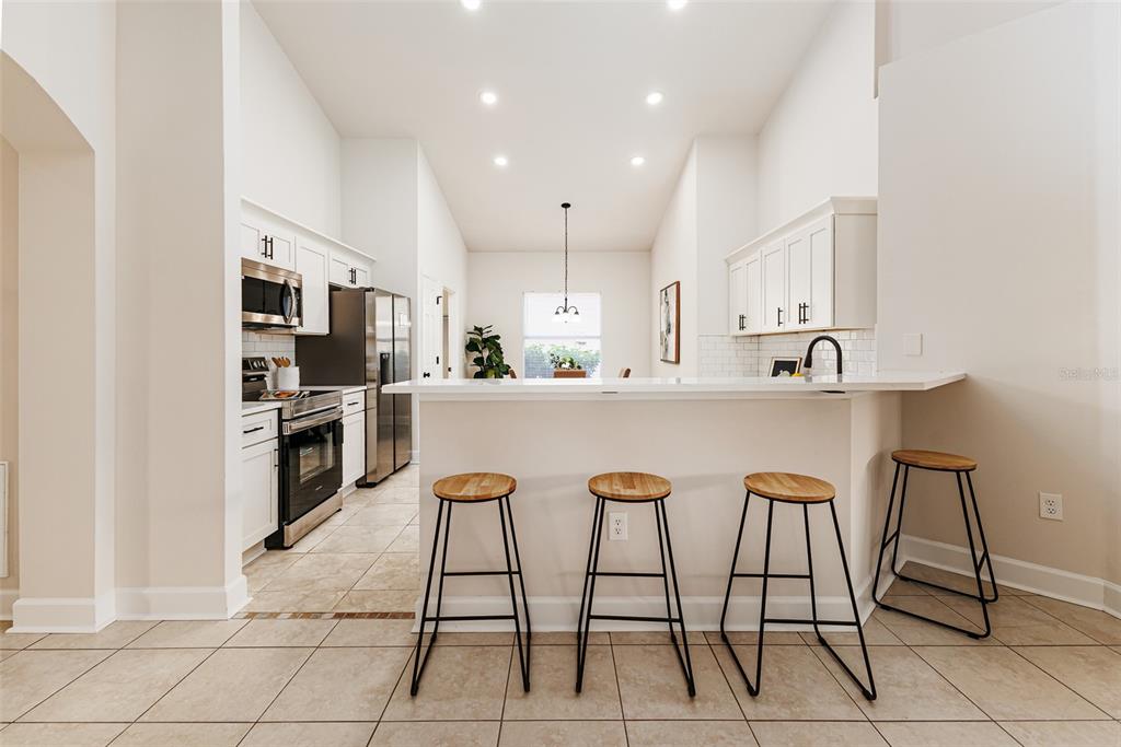 A kitchen with white cabinets, stainless steel appliances, and a breakfast bar with three stools — 1705 ALTAVISTA CIRCLE, LAKELAND, FL