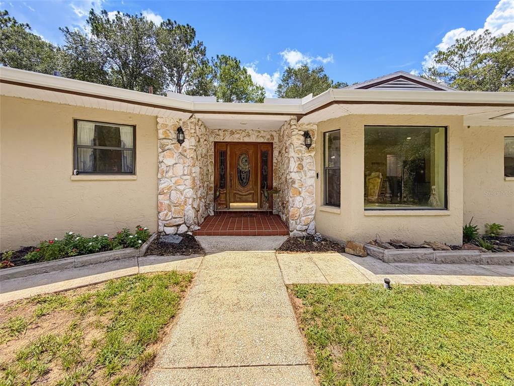 The exterior of a single-story house features a stone-accented entryway and a large picture window — 26311 WILLOW STREET, BROOKSVILLE, FL