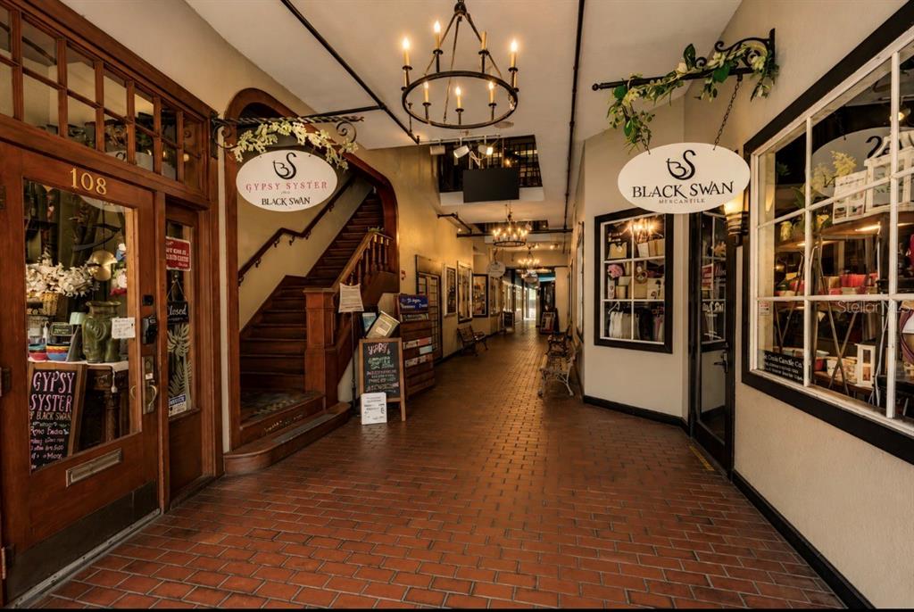 A brick-floored indoor hallway features storefronts, a wooden staircase, and hanging chandeliers — 411 N DONNELLY ST, MOUNT DORA, FL