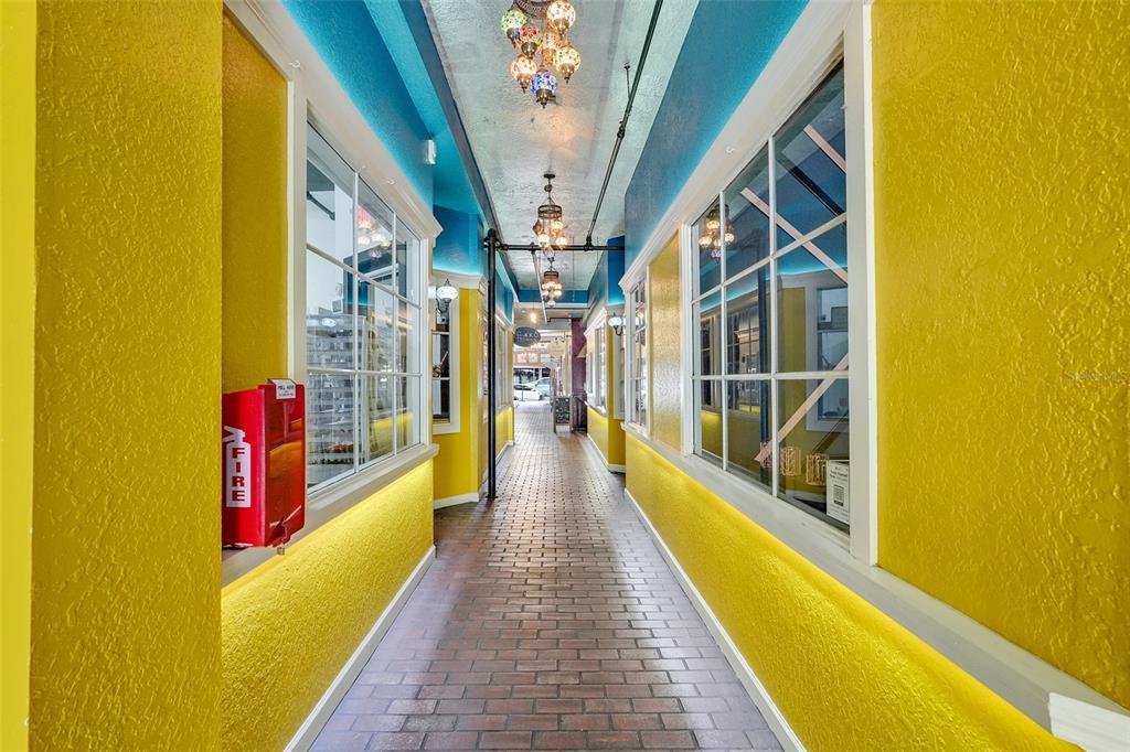 A narrow outdoor walkway with yellow walls, brick flooring, and decorative hanging lights — 411 N DONNELLY ST, MOUNT DORA, FL