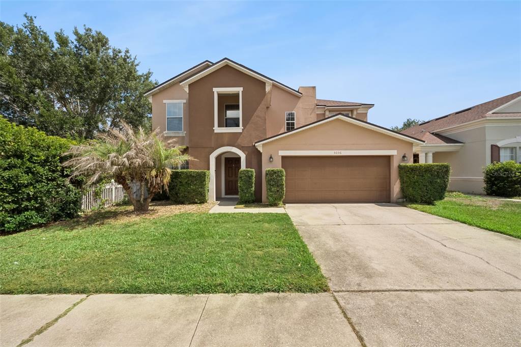 A two-story suburban house features a brown stucco exterior, a two-car garage, and landscaping — 5056 GANDROSS LANE, MOUNT DORA, FL