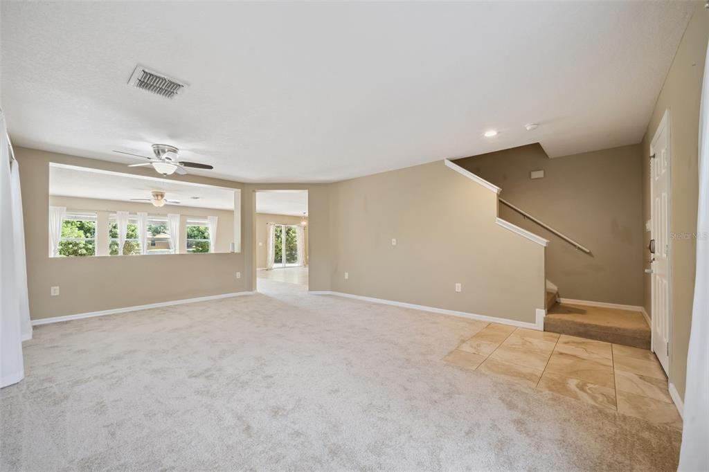 A spacious living room features beige carpet, tan walls, a staircase, and a large window opening — 5056 GANDROSS LANE, MOUNT DORA, FL