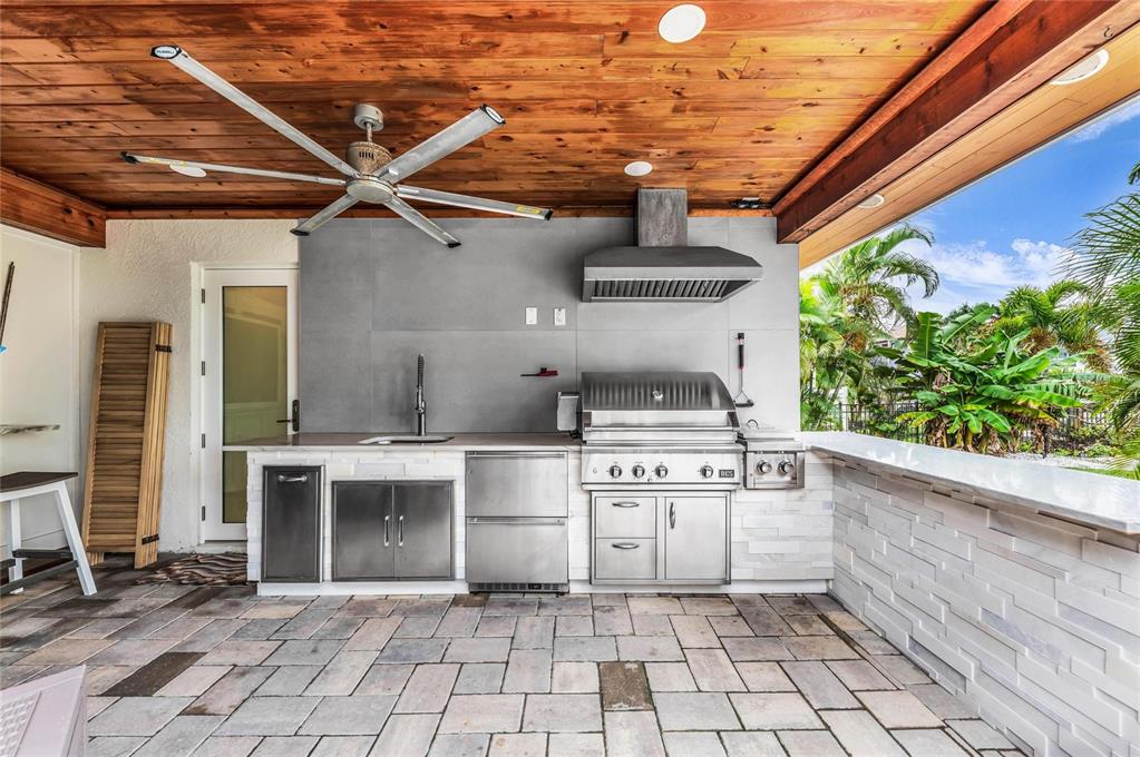 An outdoor kitchen features a stainless steel grill, sink, and stone facade under a wood ceiling — 714 NORTON STREET, LONGBOAT KEY, FL
