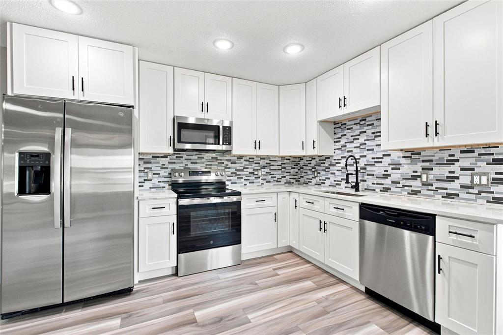 A modern kitchen features white cabinets, stainless steel appliances, and a multi-colored tile backsplash — 6273 TORONJA DRIVE, INDIAN LAKE ESTATES, FL