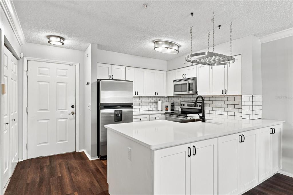 A kitchen features white cabinets, stainless steel appliances, a subway tile backsplash, and a white island — 2400 FEATHER SOUND DRIVE UNIT 133, CLEARWATER, FL
