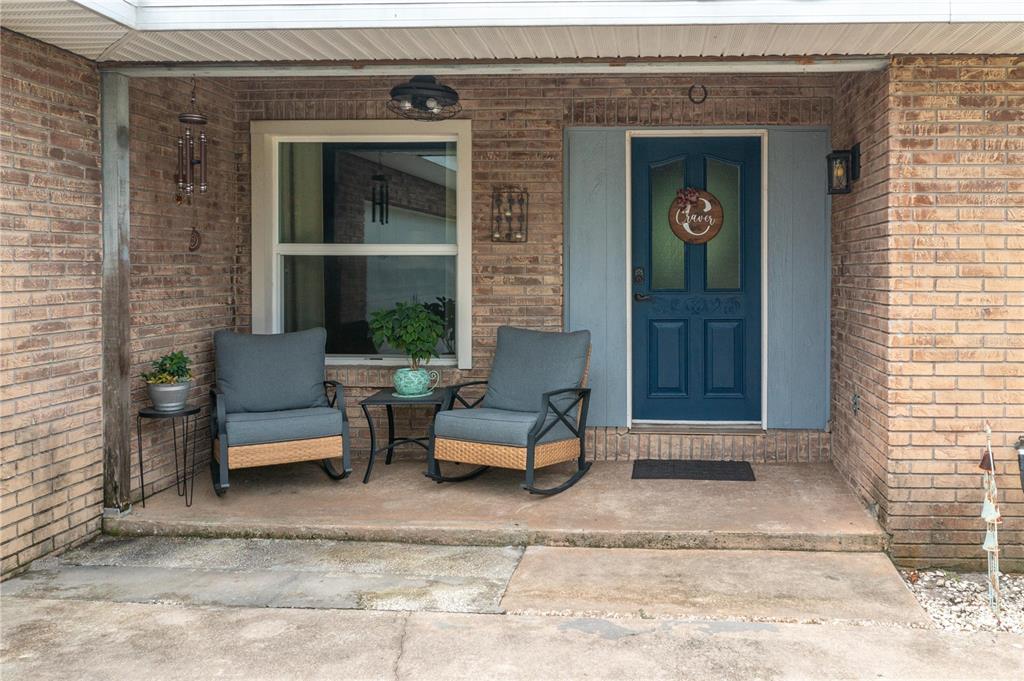A brick-front porch features two rocking chairs, a small table, and a blue front door — 1755 BETH LANE, WINTER HAVEN, FL