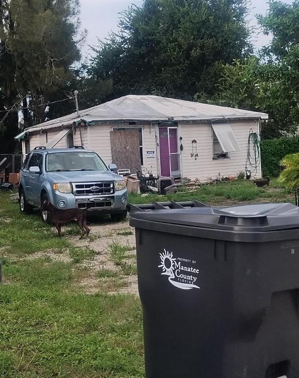 A light-colored, single-story house with a boarded-up window, a purple door, and a parked SUV — 1305 & 1309 HARDIN AVENUE, SARASOTA, FL