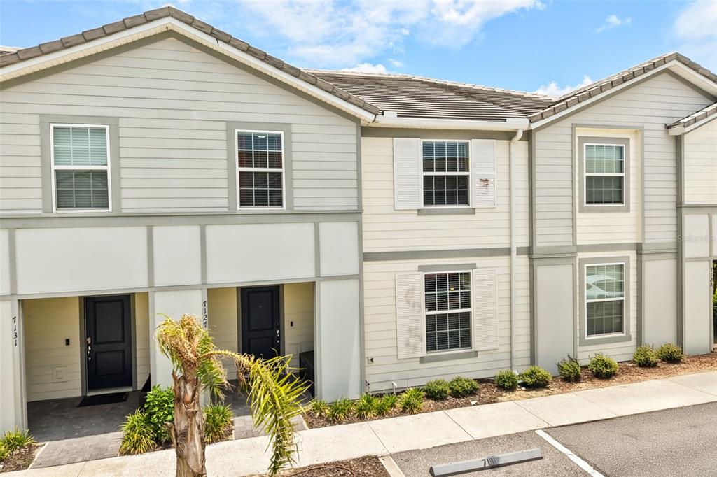 The exterior of a two-story townhouse features light-colored siding, dark doors, and a small garden — 7127 OAKMOSS LOOP, DAVENPORT, FL