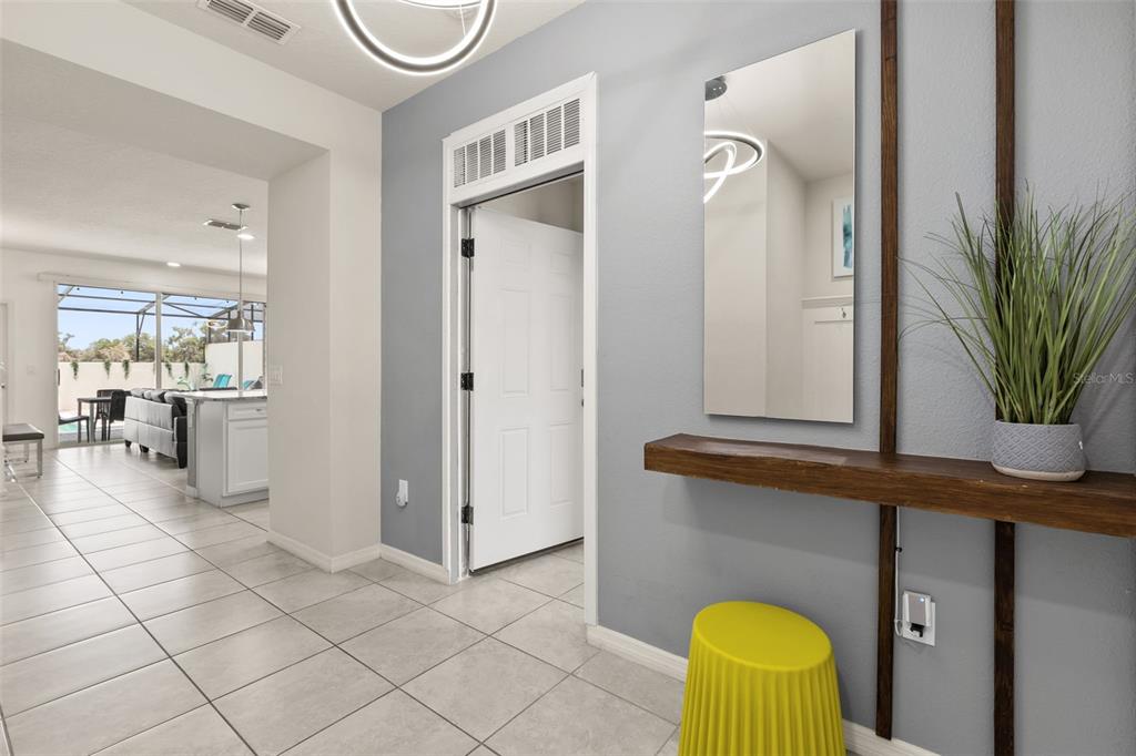 A tiled entryway features a floating wooden shelf, a mirror, and a yellow stool — 7127 OAKMOSS LOOP, DAVENPORT, FL