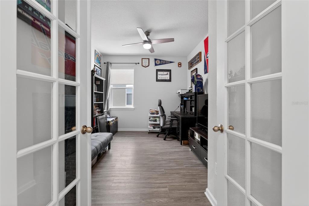 A home office with wood-look flooring, a ceiling fan, and double glass-paneled entry doors — 12273 BLUE PACIFIC DRIVE, RIVERVIEW, FL