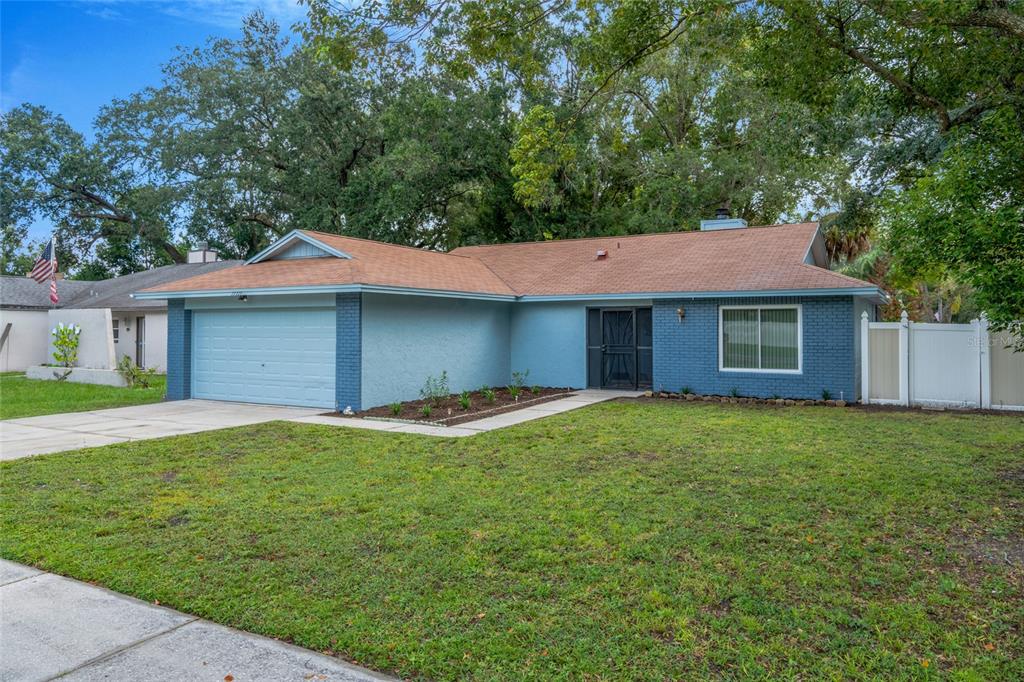 A single-story blue brick house with a brown shingled roof and a two-car garage — 17717 CRANBROOK DRIVE, LUTZ, FL
