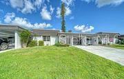 A single-story house with a flat roof, carport, and a grassy front lawn under blue skies — 3961 ASHWOOD LANE UNIT 44, SARASOTA, FL
