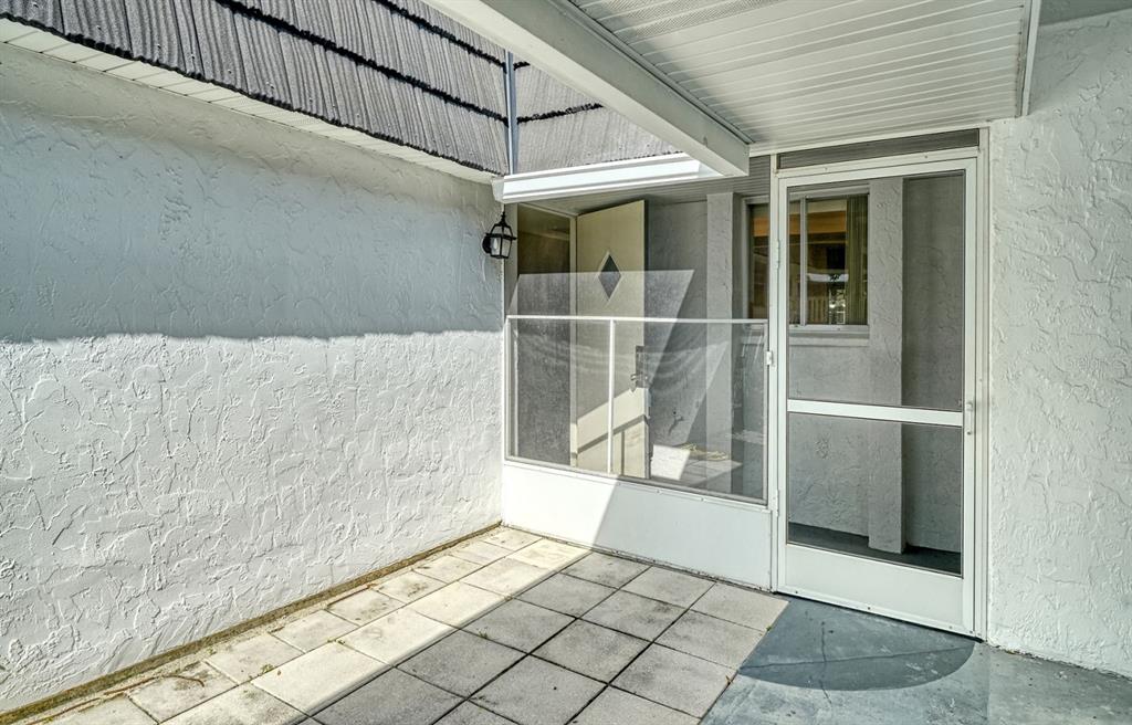 A covered patio features white stucco walls, square concrete pavers, and a screen door entrance — 3961 ASHWOOD LANE UNIT 44, SARASOTA, FL