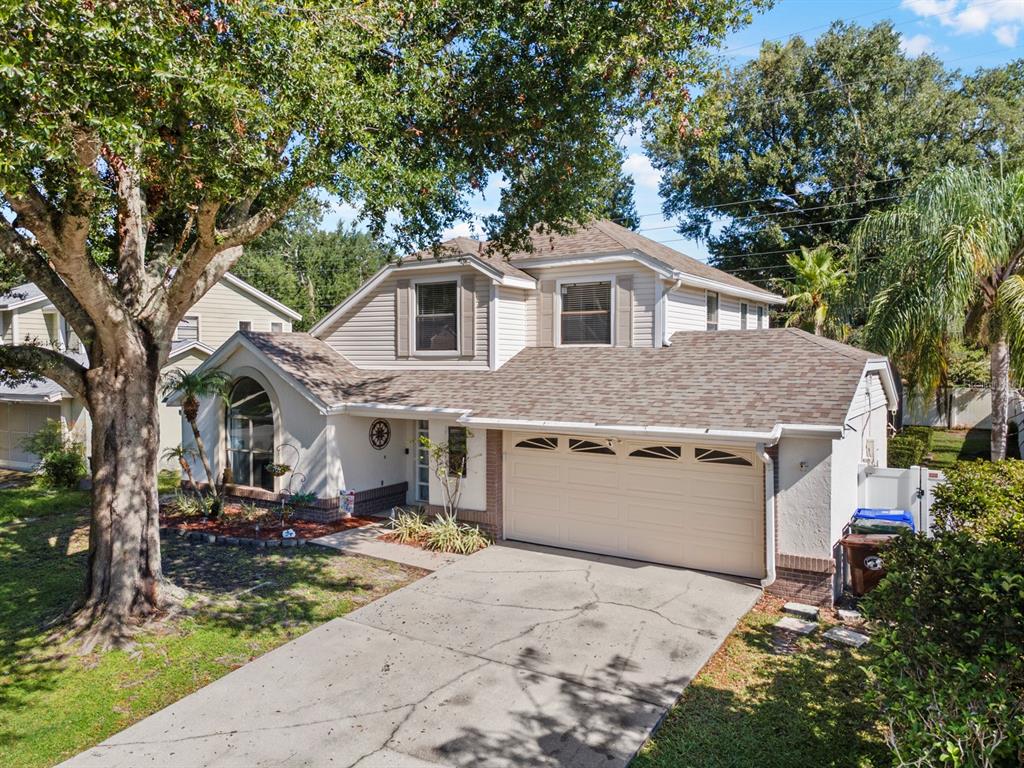 An exterior view of a two-story suburban house with a concrete driveway and large tree — 1461 AMANDA ROAD, KISSIMMEE, FL