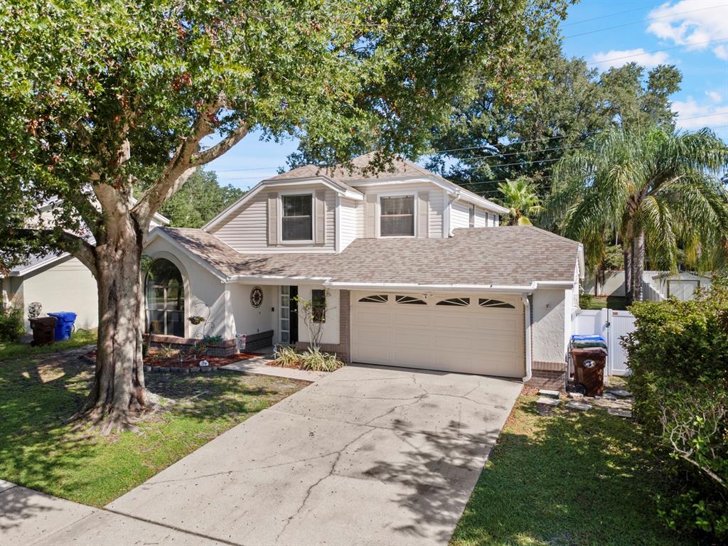 A two-story suburban house with a beige exterior, a two-car garage, and a large tree — 1461 AMANDA ROAD, KISSIMMEE, FL