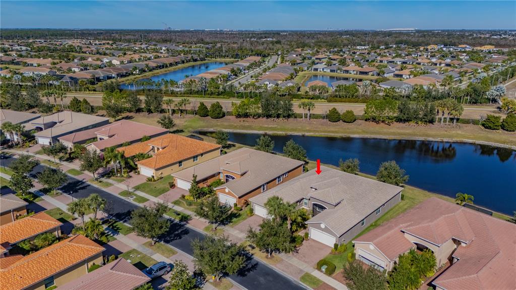 An aerial view shows a suburban neighborhood with houses bordering a long, narrow lake — 15644 AURORA LAKE CIRCLE, WIMAUMA, FL