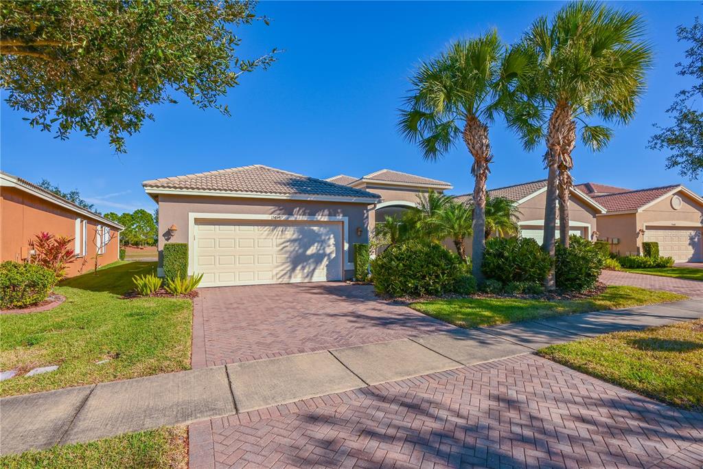 A single-story house with a two-car garage, palm trees, and a paved driveway — 15644 AURORA LAKE CIRCLE, WIMAUMA, FL