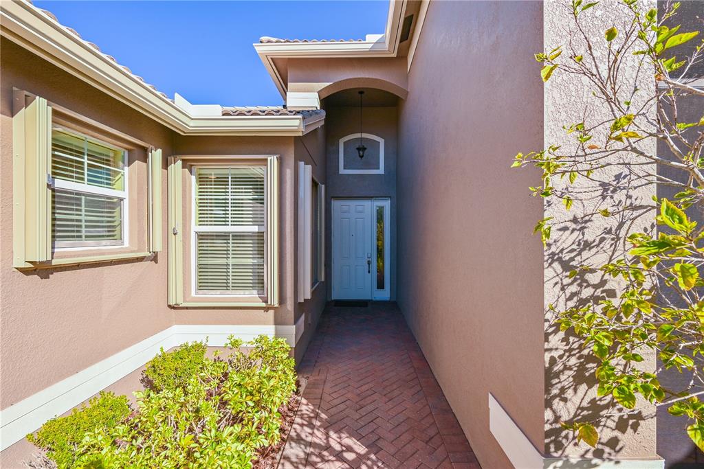 A brick walkway leads to the front entrance of a house with beige stucco walls — 15644 AURORA LAKE CIRCLE, WIMAUMA, FL