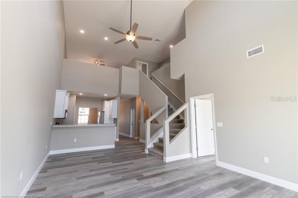 A living area with high ceilings, wood-look flooring, and a staircase leading to a loft — 1942 OASIS BOULEVARD UNIT 1942, SEBRING, FL