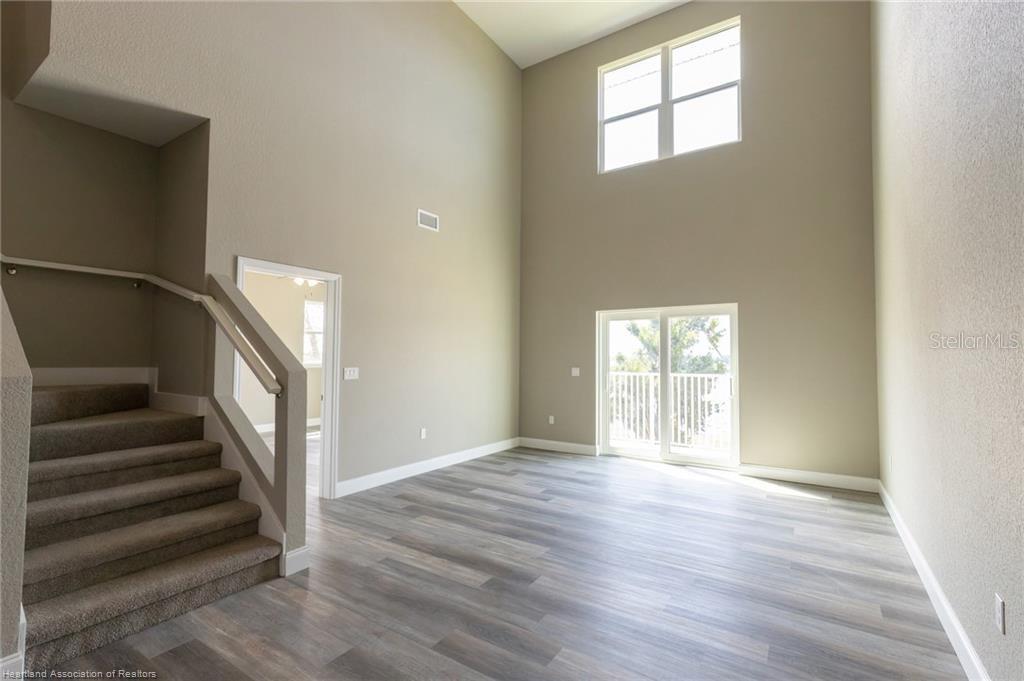 A living room features high ceilings, wood-look flooring, carpeted stairs, and a sliding glass door — 1942 OASIS BOULEVARD UNIT 1942, SEBRING, FL