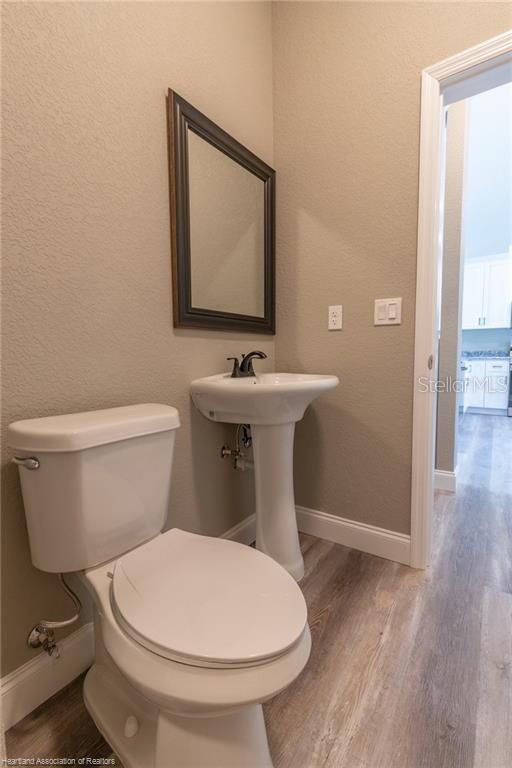 A half bathroom features a white pedestal sink, a toilet, and a framed wall mirror — 1942 OASIS BOULEVARD UNIT 1942, SEBRING, FL