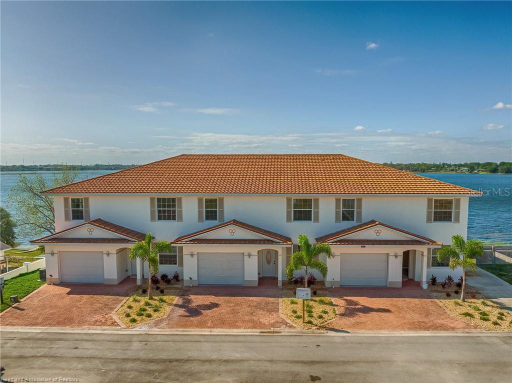 A two-story, three-unit townhouse with a tile roof and brick driveway sits by a lake — 1942 OASIS BOULEVARD UNIT 1942, SEBRING, FL