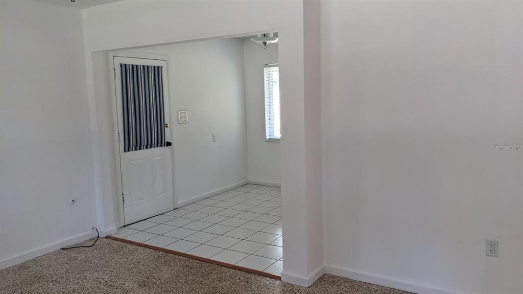 A room with carpeted flooring transitions into a tiled area featuring a white exterior door — 2104 PALM TERRACE, SARASOTA, FL