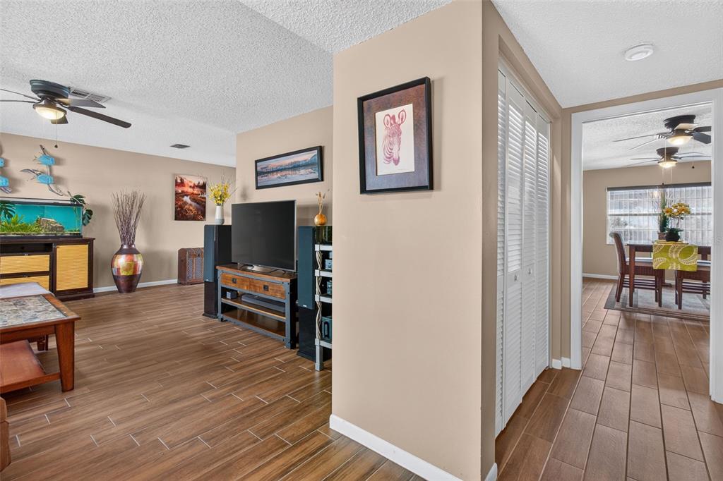 A living room with wood-look tile floors, a television console, and a dining area beyond — 2221 COLONIAL DRIVE, DUNEDIN, FL