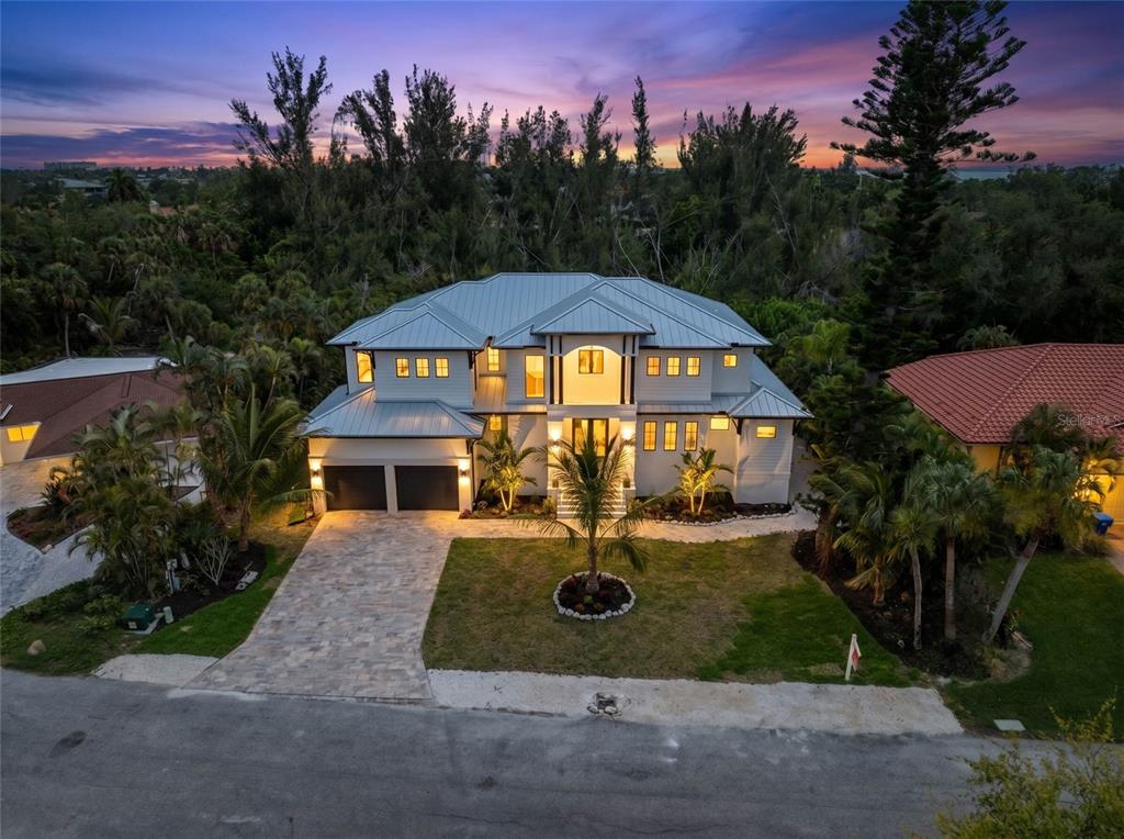 An aerial view of a two-story house with a metal roof and paved driveway at dusk — 626 BUTTONWOOD DRIVE, LONGBOAT KEY, FL