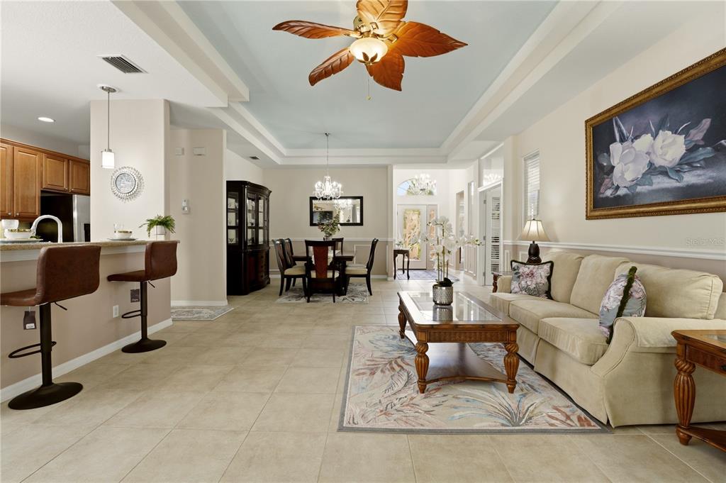 An open-concept living and dining area features tile floors, a tray ceiling, and neutral decor — 2156 MESIC HAMMOCK WAY, VENICE, FL