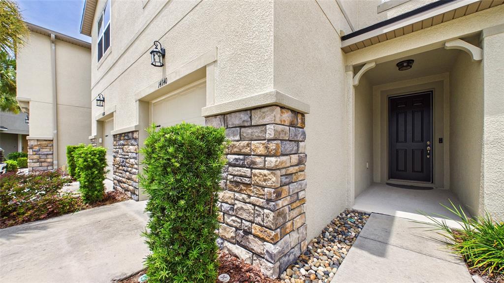 A residential exterior view featuring a stone-accented corner, a dark front door, and landscaping — 14140 DAMSELFLY DRIVE, TAMPA, FL