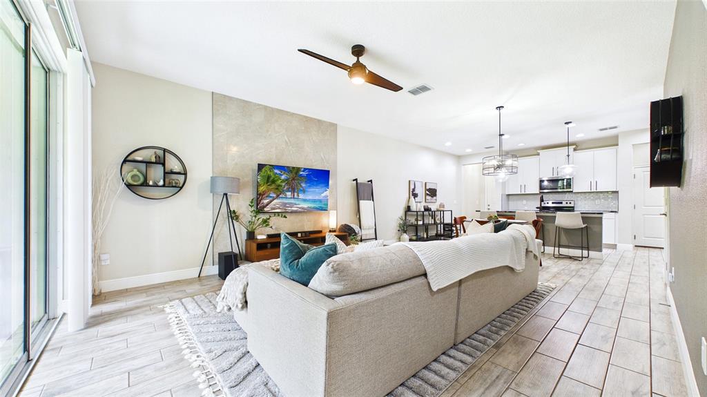 A living room with light tile floors, a sofa, and a wall-mounted television — 14140 DAMSELFLY DRIVE, TAMPA, FL