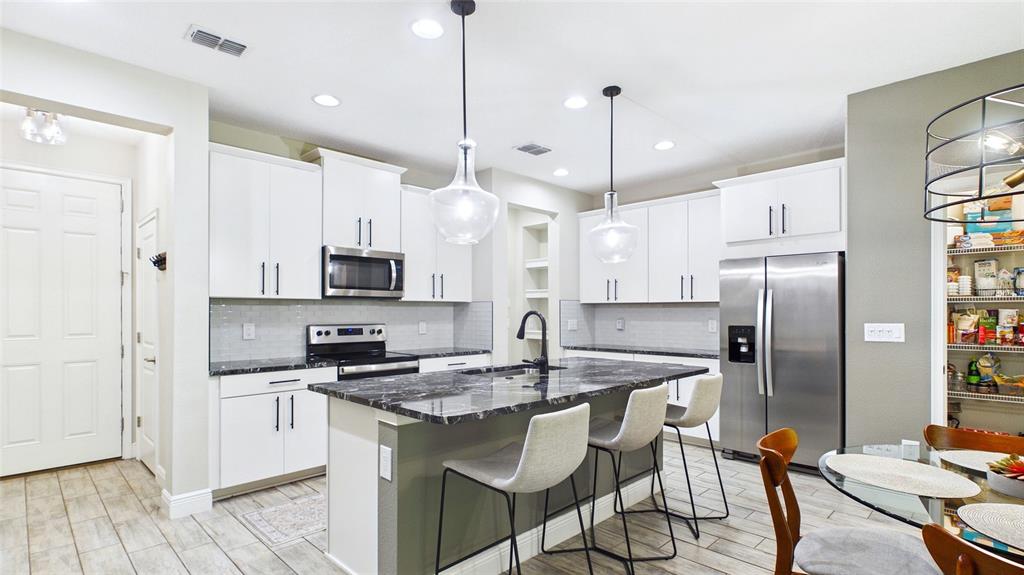A modern kitchen features white cabinets, a dark marble island, and stainless steel appliances — 14140 DAMSELFLY DRIVE, TAMPA, FL