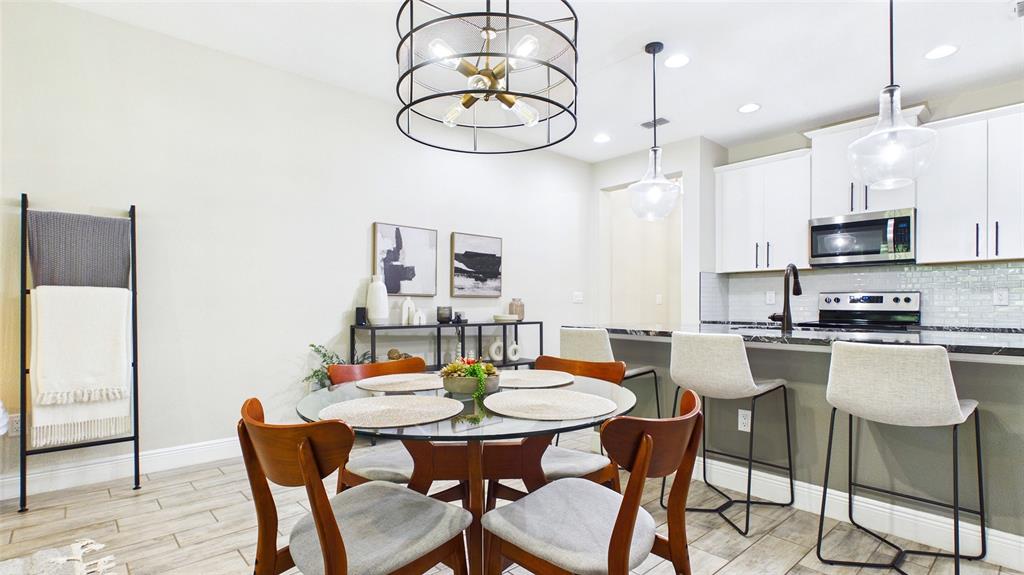 A dining area with a glass table and a kitchen with white cabinets and stools — 14140 DAMSELFLY DRIVE, TAMPA, FL