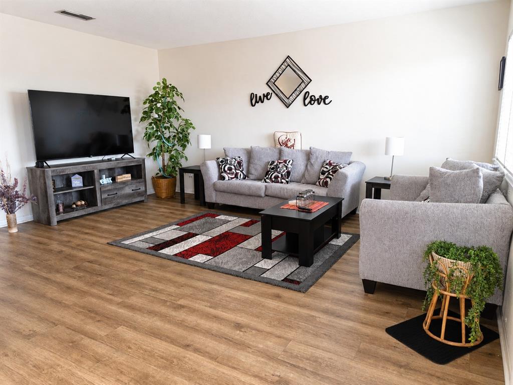 A living room features gray sofas, a television on a console, and wood-look flooring — 11251 80TH AVENUE UNIT 306, SEMINOLE, FL