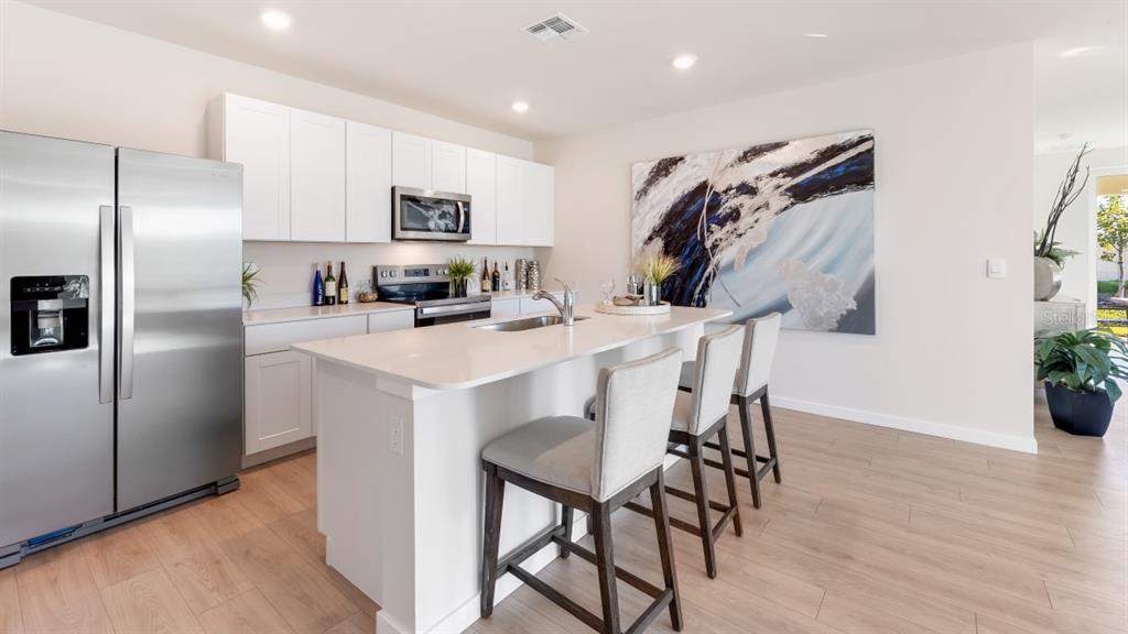 A modern kitchen features white cabinetry, stainless steel appliances, a central island, and bar stools — 4583 SCHUBERT TRAIL, NORTH PORT, FL
