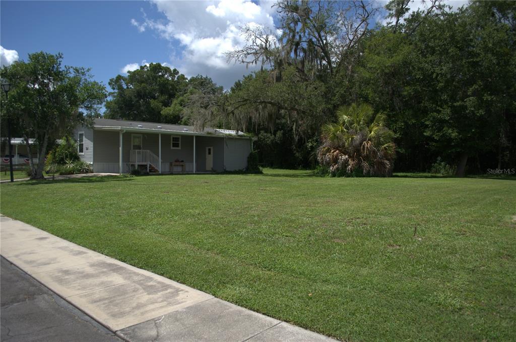 A single-story house with a covered porch sits on a large, grassy lot with trees — MULLER DRIVE, ZEPHYRHILLS, FL