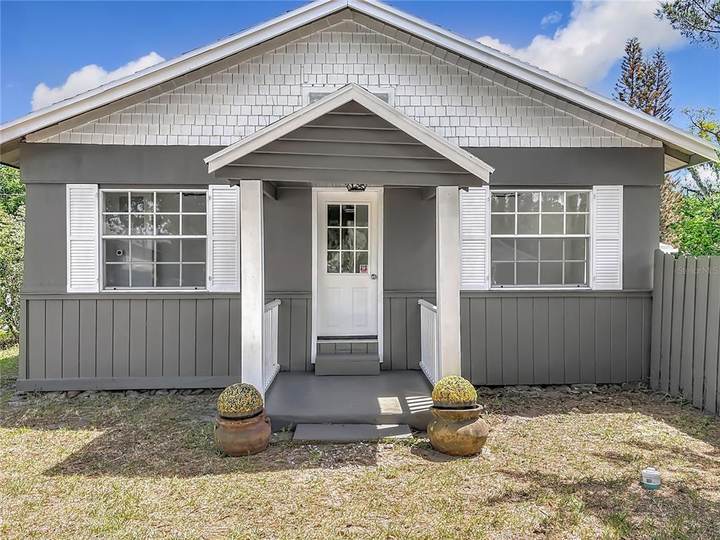 The exterior of a gray house features a gabled porch, white shutters, and two potted plants — 265 NEWCOMB STREET, NEW SMYRNA BEACH, FL