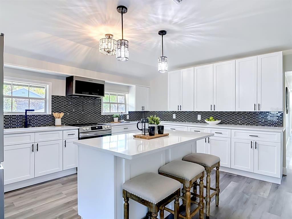 A modern kitchen features white cabinets, a central island with stools, and a black backsplash — 265 NEWCOMB STREET, NEW SMYRNA BEACH, FL