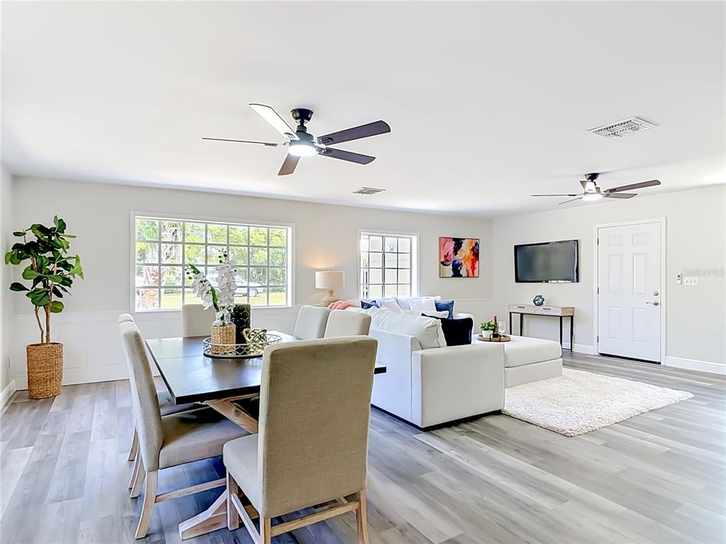 An open-concept living and dining area features light wood-look flooring, white walls, and two ceiling fans — 265 NEWCOMB STREET, NEW SMYRNA BEACH, FL