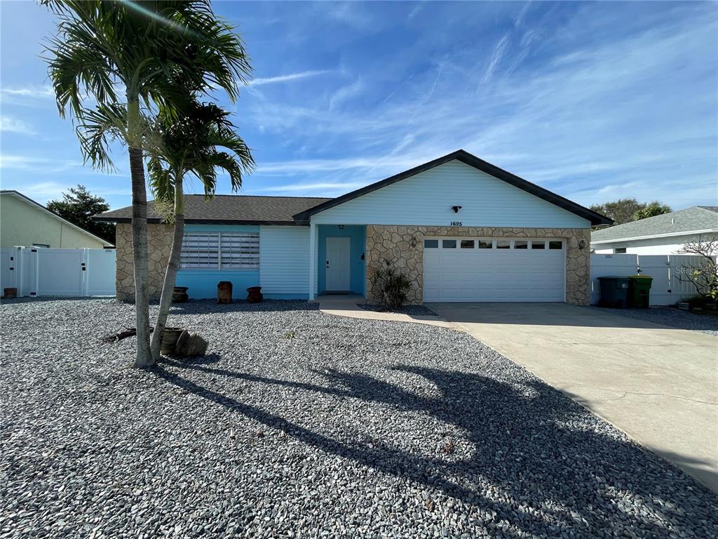 A single-story house with light blue siding, stone accents, and a gravel front yard — 1695 N BANANA RIVER DRIVE, MERRITT ISLAND, FL