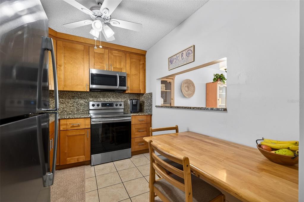 A kitchen with wood cabinets, stainless steel appliances, granite countertops, and an attached dining table — 7625 SUN ISLAND DRIVE S UNIT 207, SOUTH PASADENA, FL